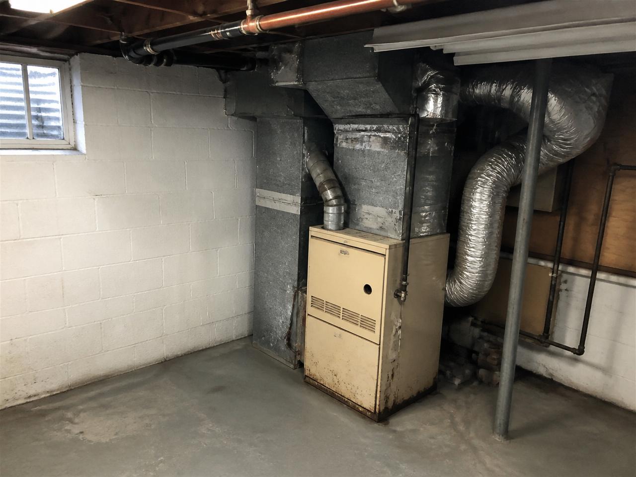 Before: Same-location before: old rusted furnace and messy ductwork in a basement utility corner